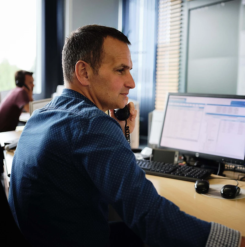 telefonierender Mitarbeiter an einem Schreibtisch mit Bildschirmen